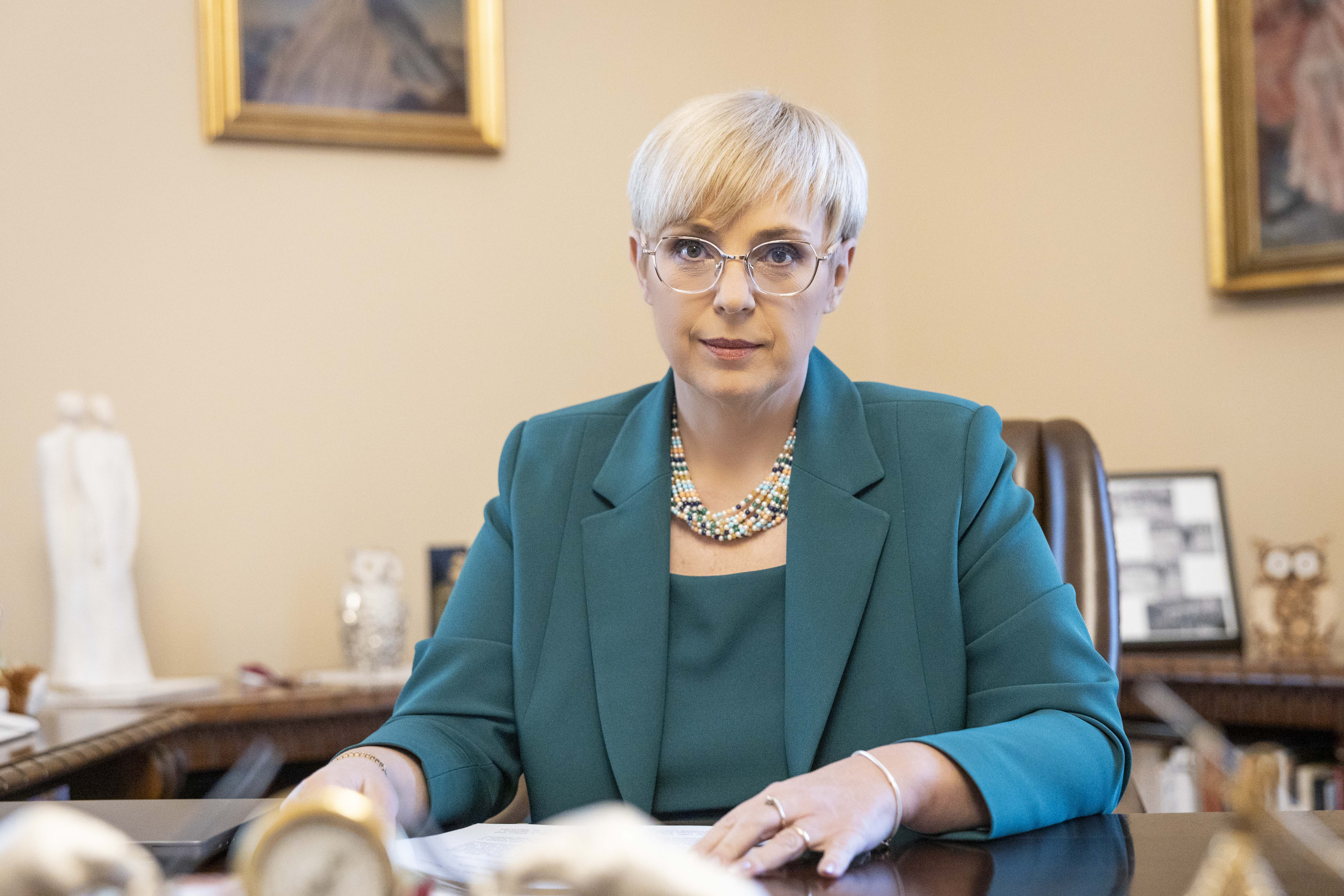 Portrait of President Pirc Musar, wearing green smart clothes, sitting behind her desk in her office.