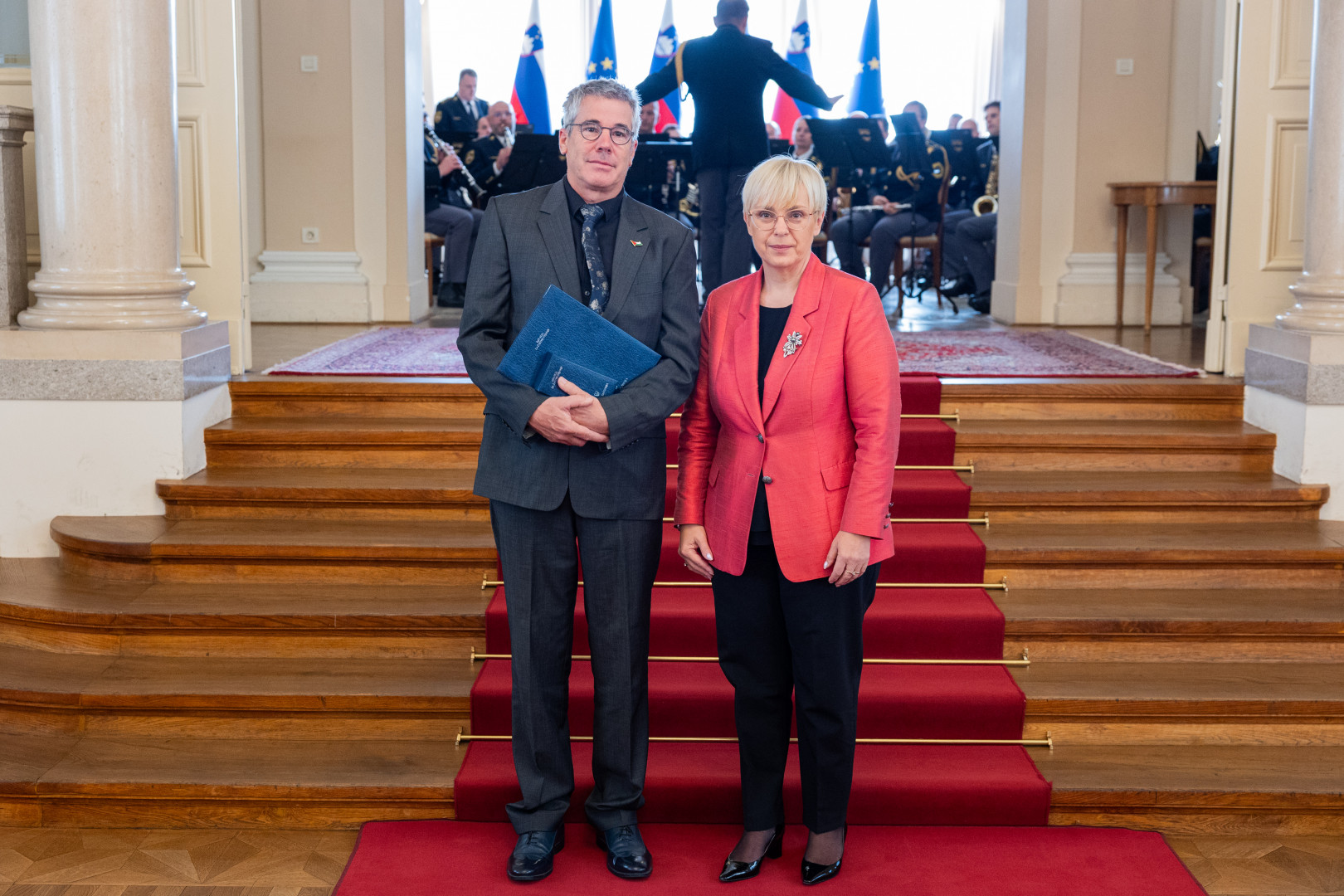 Predsednica stoji pod stopnicami z odlikovancem Tomom Potokarjem.