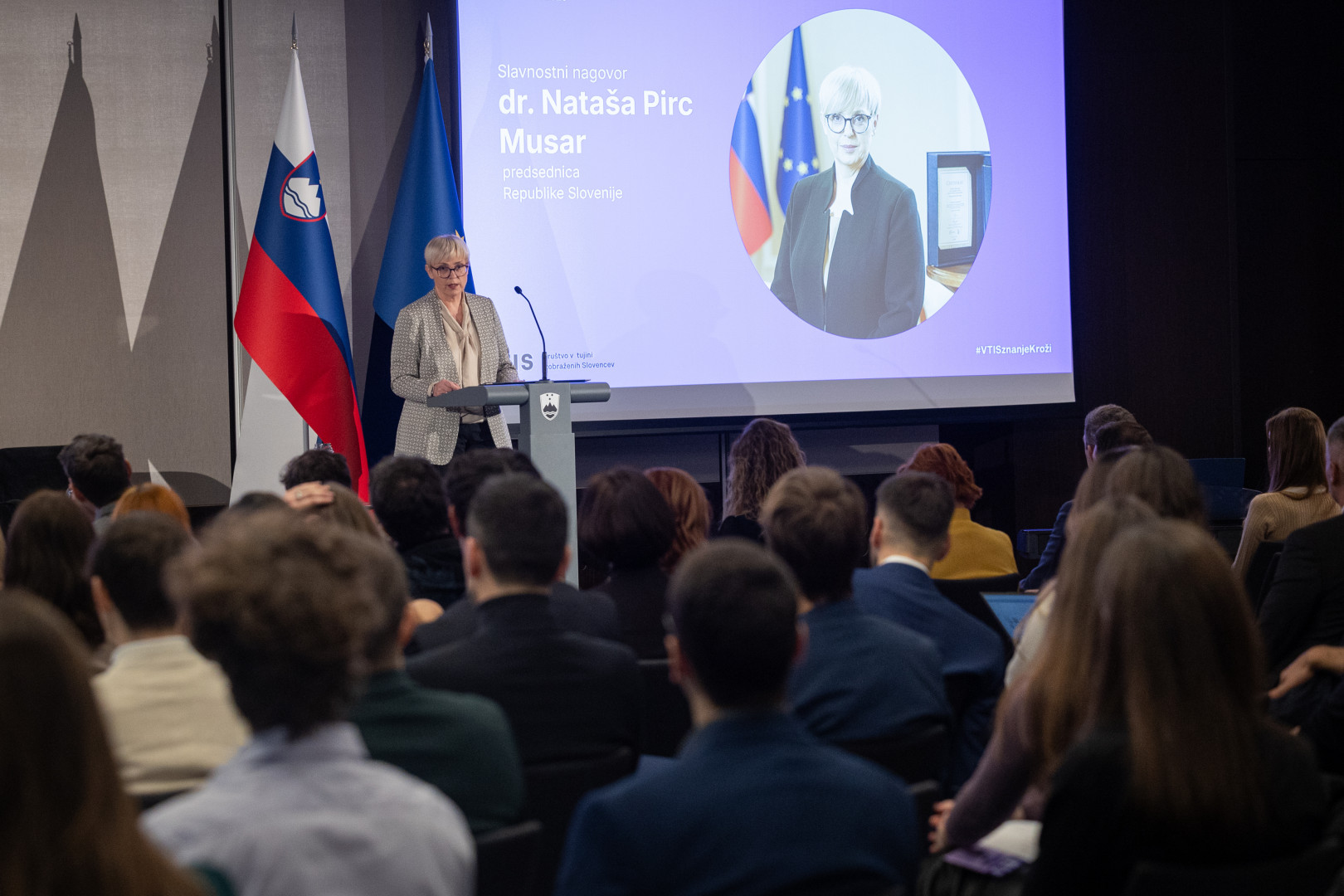 Predsednica stoji na odru za govornico in nagovarja zbrane na dogodku.