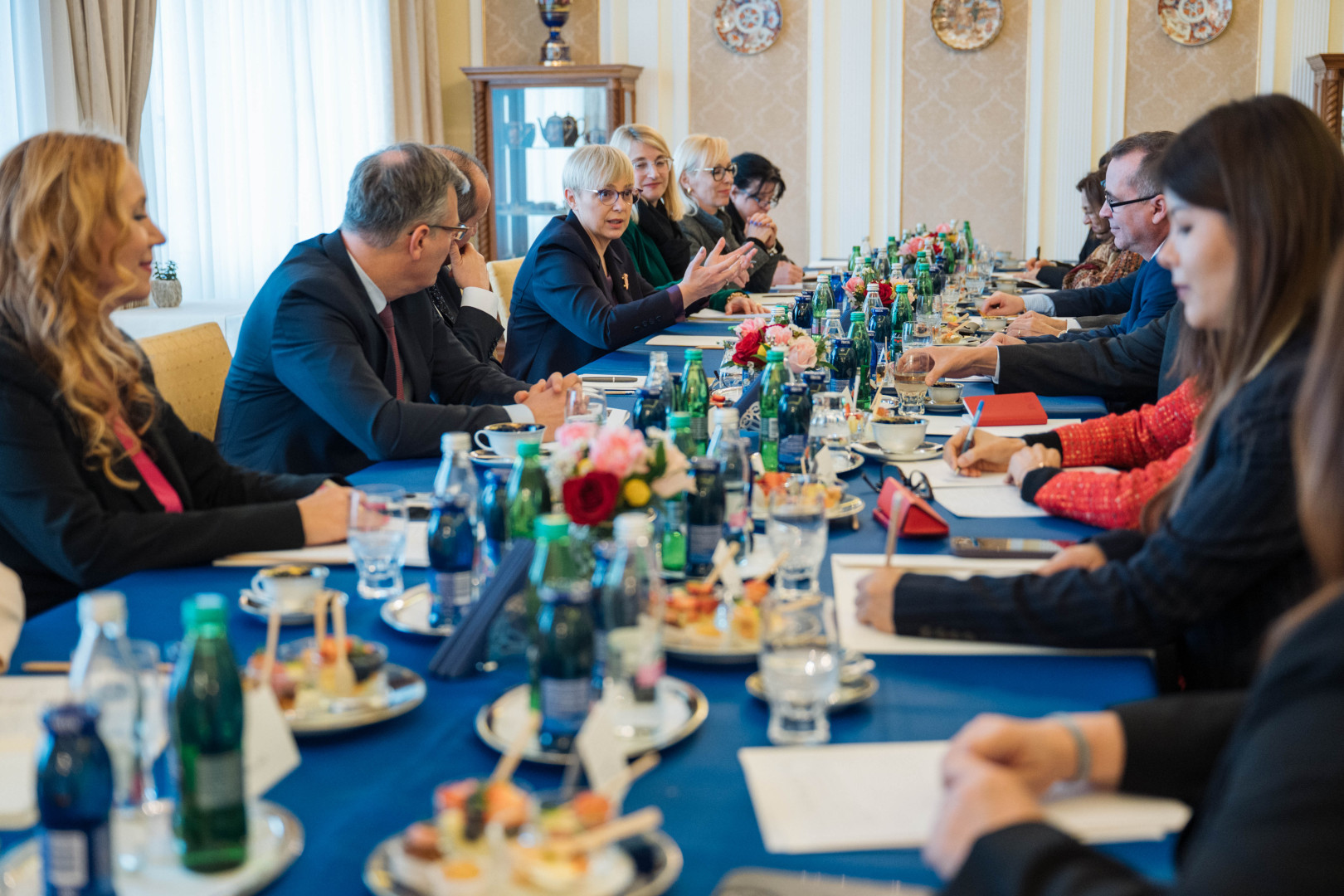 Predsednica sedi za mizo in govori z udeleženci srečanja, okoli nje sedijo ambasadorji