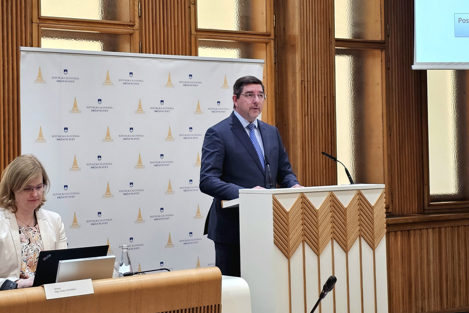 Soprog izza govornice nagovarja zbrane na posvetu v Državnem svetu.