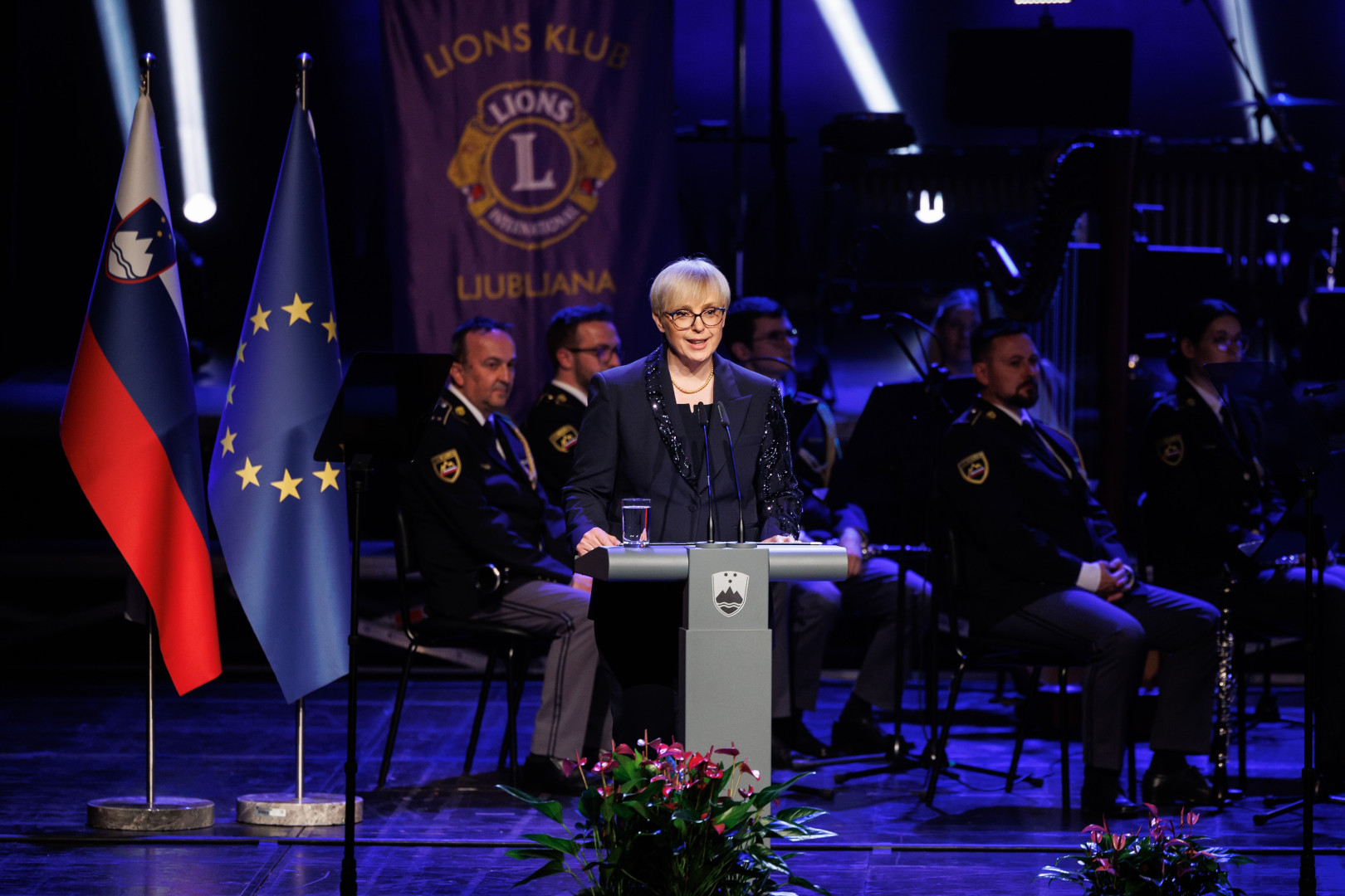 Predsednica stoji za govornico in nagovarja zbrane na koncertu.