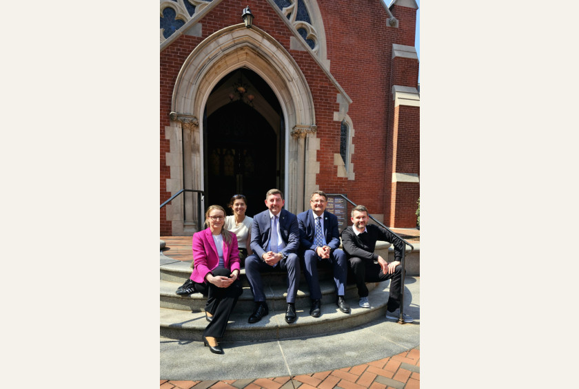 Skupina petih ljudi sedi na stopnicah pred cerkvenim vhodom.