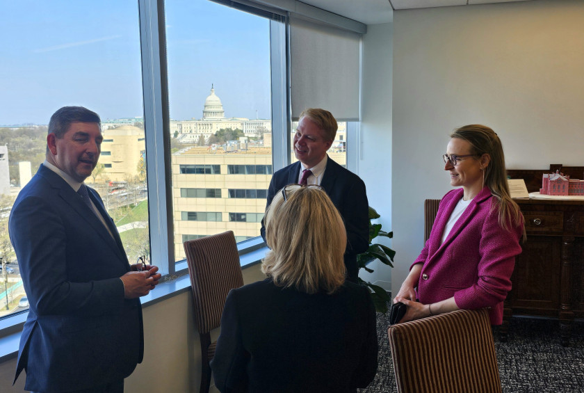 Dr. Musar in še tri osebe stojijo ob oknu in se pogovarjajo, v ozadju je Kapitol.