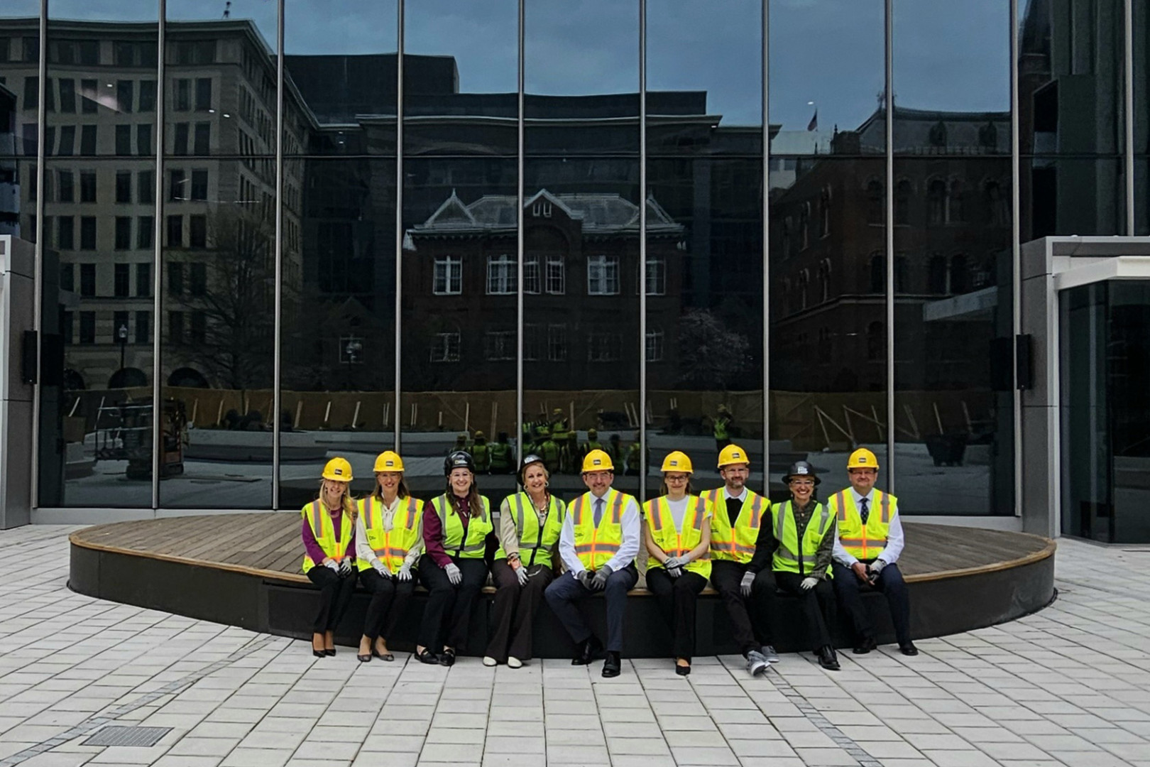 Skupina ljudi v zaščitni opremi sedi pred moderno stavbo s stekleno fasado.