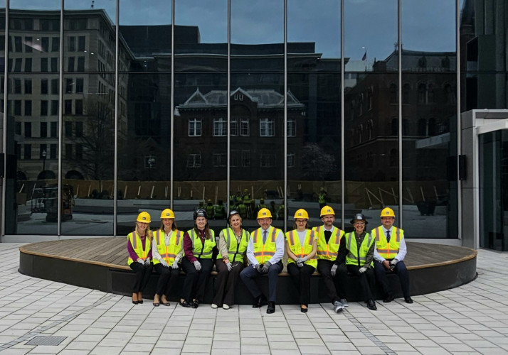 Skupina ljudi v zaščitni opremi sedi pred moderno stavbo s stekleno fasado.