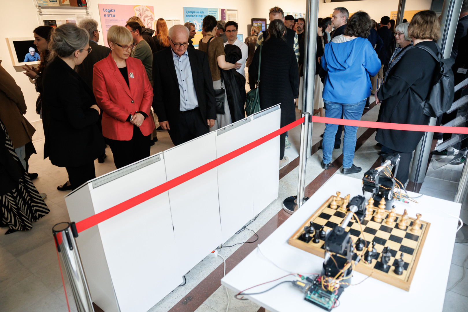 Predsednica stoji pred razstavnim eksponatom, kjer dva robota igrata šah.