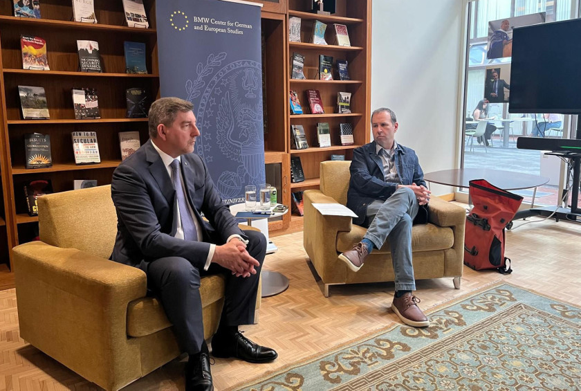 Dr. Musar se pogovarja z moškim v naslanjačih v knjižnici ali študijskem prostoru.