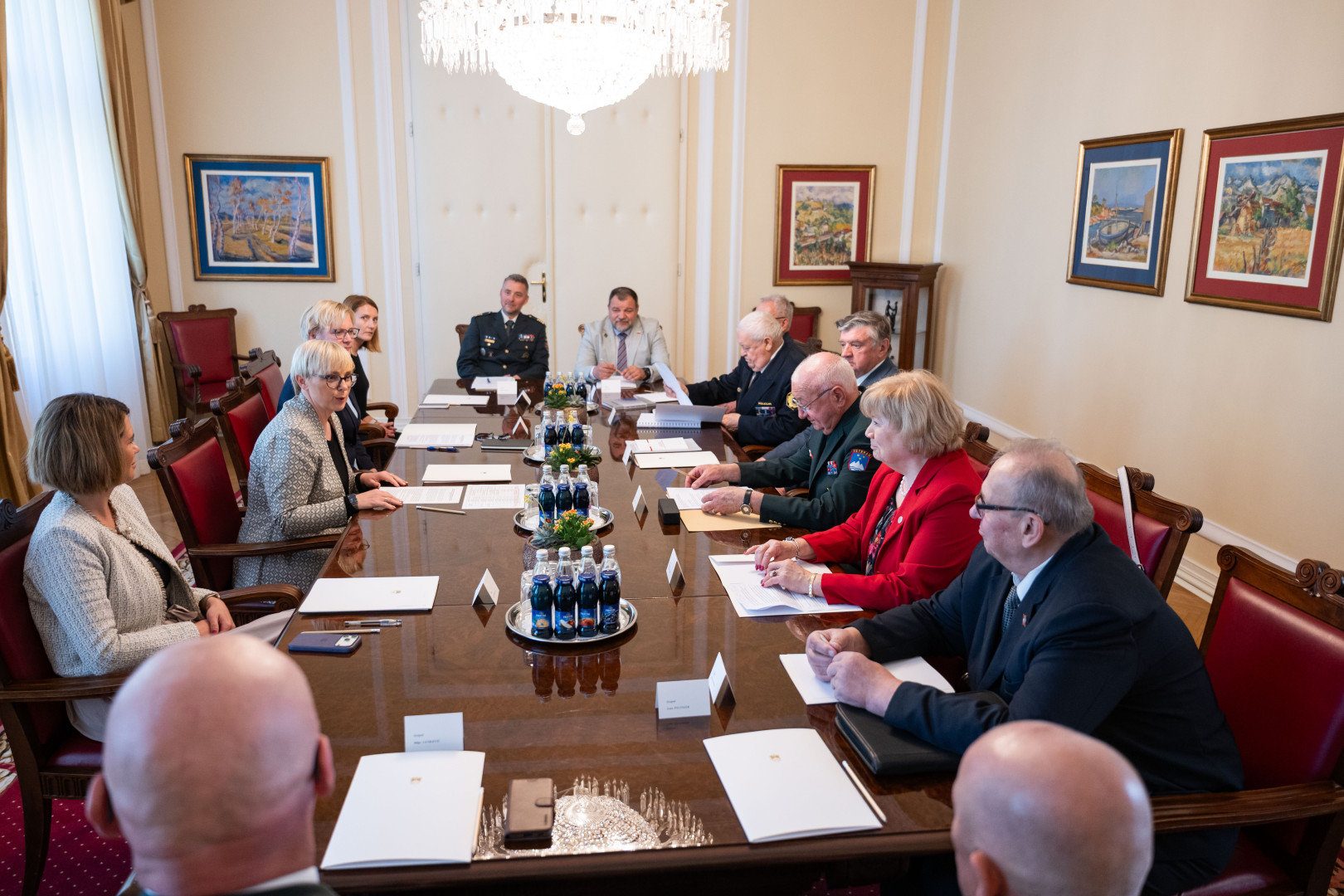 Predsednica sedi za mizo in govori z udeleženci srečanja.