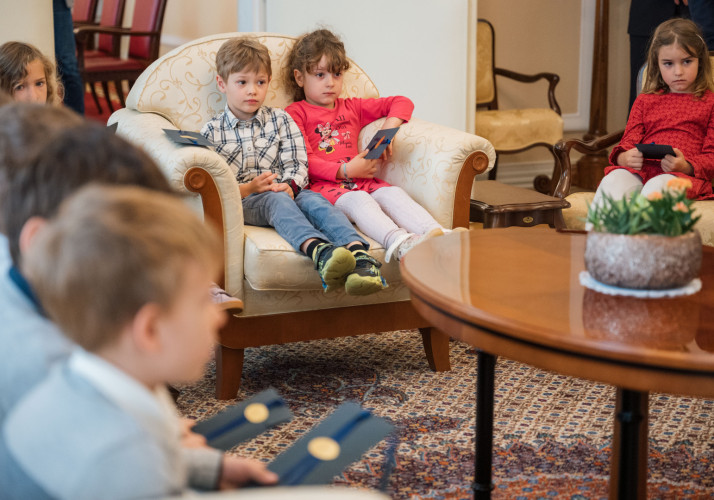 Otroci sedijo na naslanjačih v dvorani v Predsedniški palači.