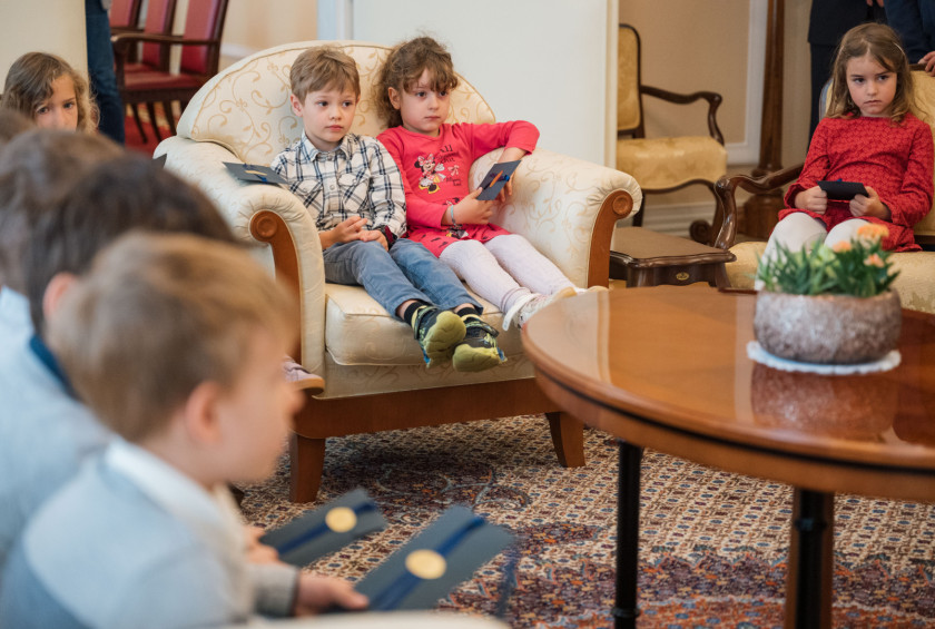 Otroci sedijo na naslanjačih v dvorani v Predsedniški palači.