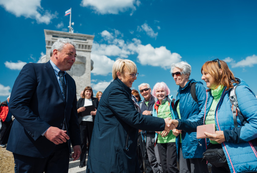 Predsednica se rokuje z udeleženko dogodka, okoli zbrani nasmejani ljudje.
