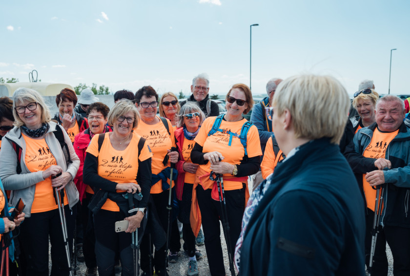 Predsednica se pogovarja s skupino pohodnikov v oranžnih majicah.