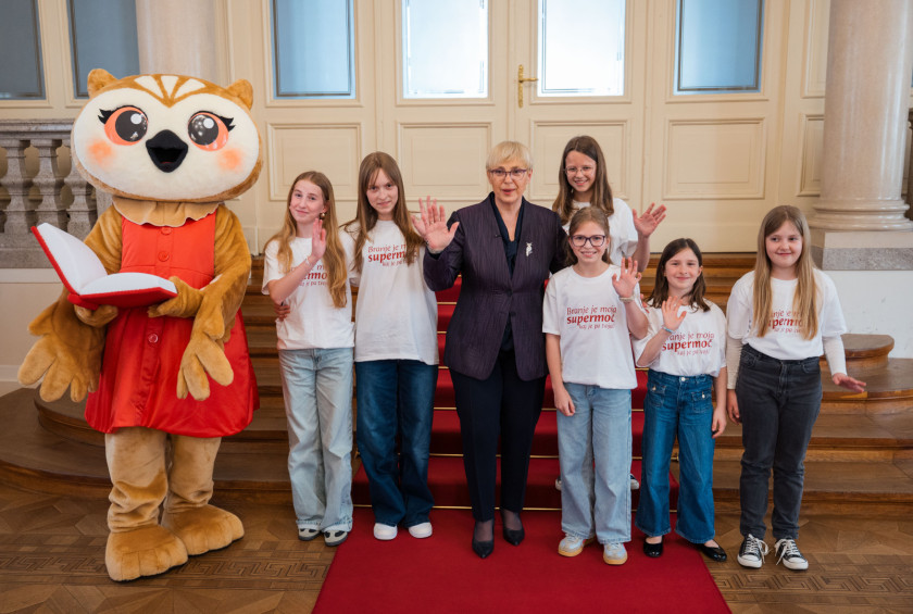 Skupinska fotografija predsednice republike s Sovico Karlo in skupino osnovnošolk, ki rade berejo. 