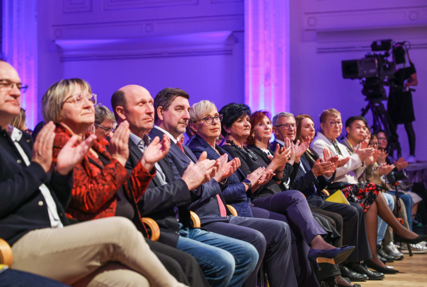 Predsednica sedi v prvi vrsti in ploska, ob njej ploskajo tudi drugi obiskovalci.