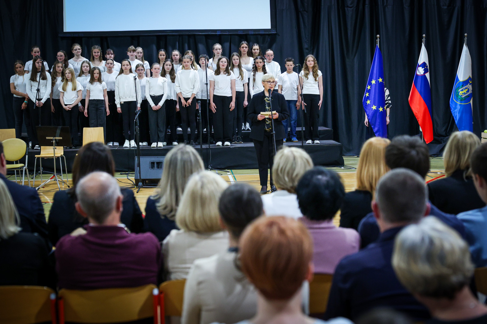 Predsednica stoji za mikrofonom in nagovarja zbrane na prireditvi.