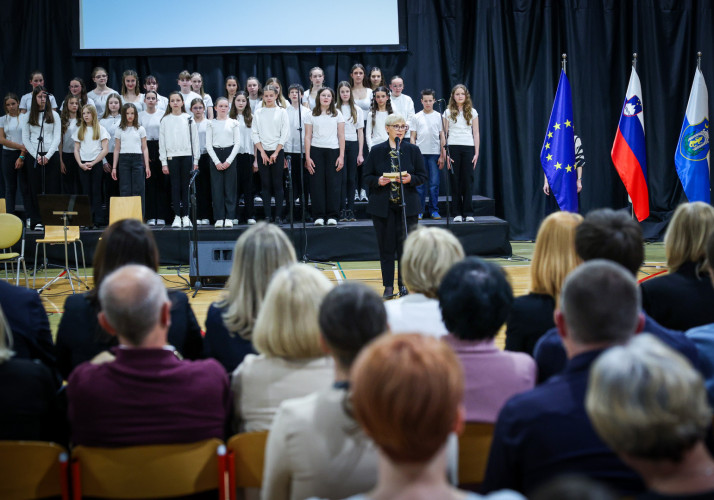 Predsednica stoji za mikrofonom in nagovarja zbrane na prireditvi.