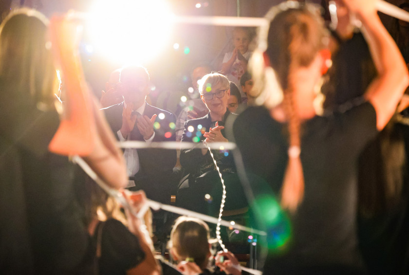 Predsednica spremlja prireditev, v rokah drži vrvico. Ozadje je osvetljeno z lučjo.