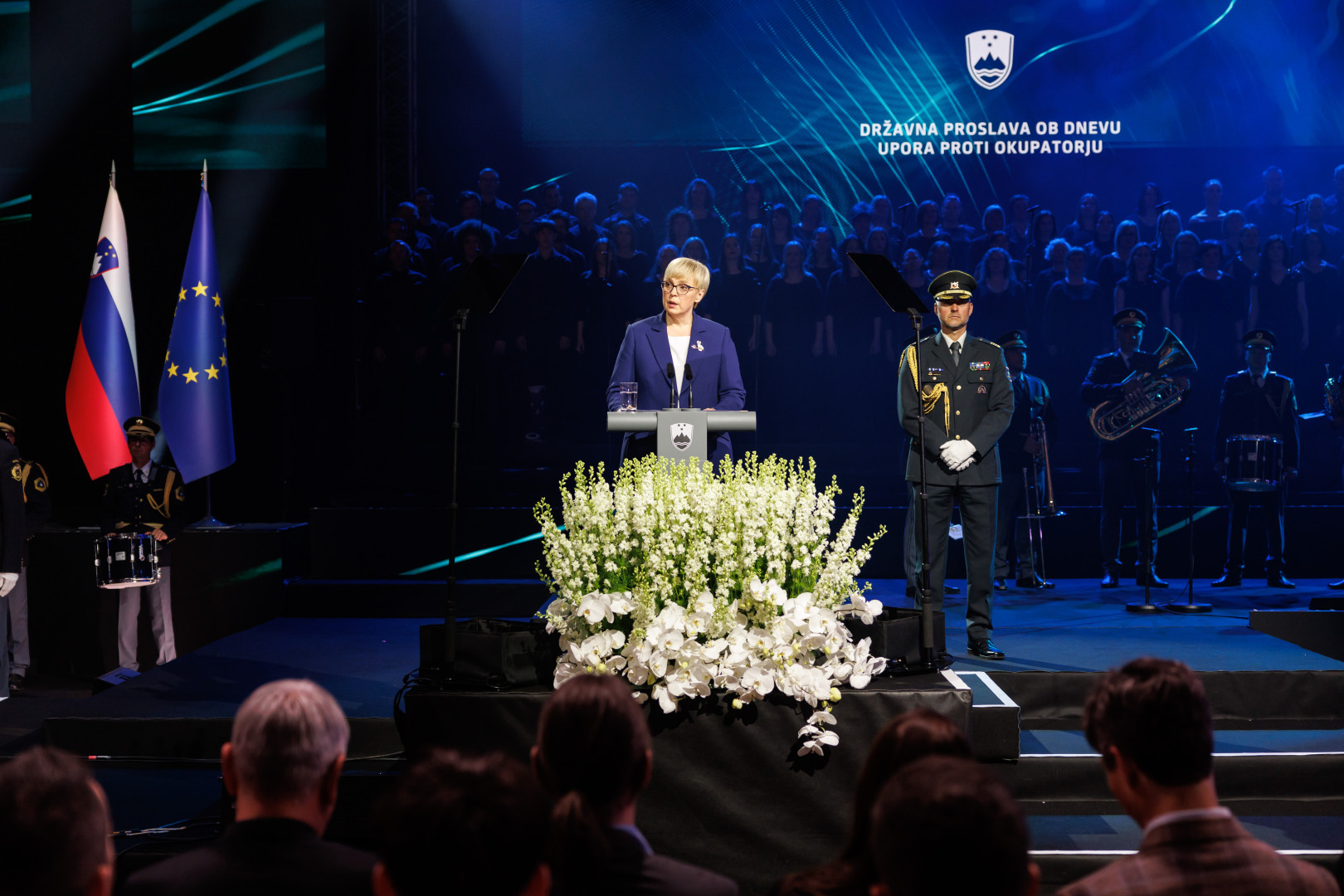 Predsednica stoji za govornico, v ozadju je napis državna proslava ob dnevu upora proti okupatorju.