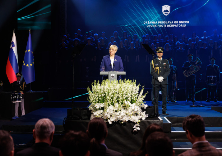 Predsednica stoji za govornico, v ozadju je napis državna proslava ob dnevu upora proti okupatorju.