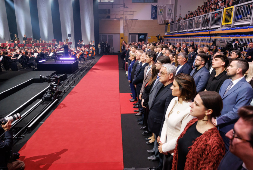 Udeleženci proslave stojijo in med predvajanjem himne na začetku proslave.