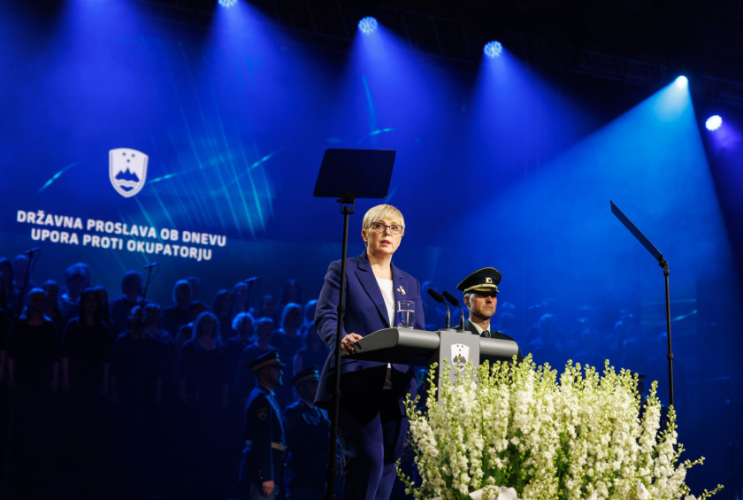 Predsednica stoji za govornico, v ozadju je napis državna proslava ob dnevu upora proti okupatorju.