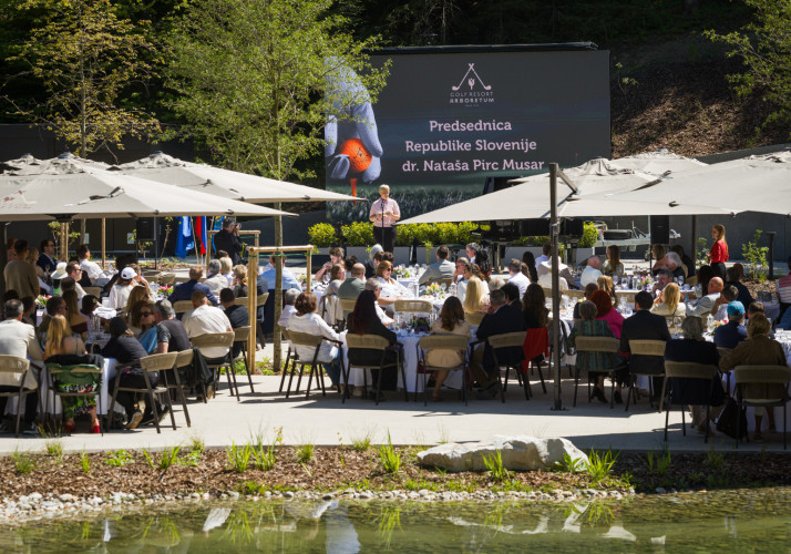Pogled na zbrane na odprtju novega golf igrišča, predsednica v ozadju stoji na odru.