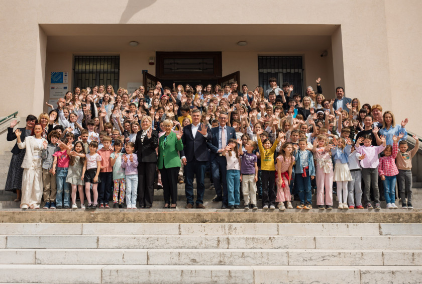 Skupinska fotografija predsednice in predsednika ter ogromnega števila šolarjev, ki stojijo na stopnicah pred šolo.