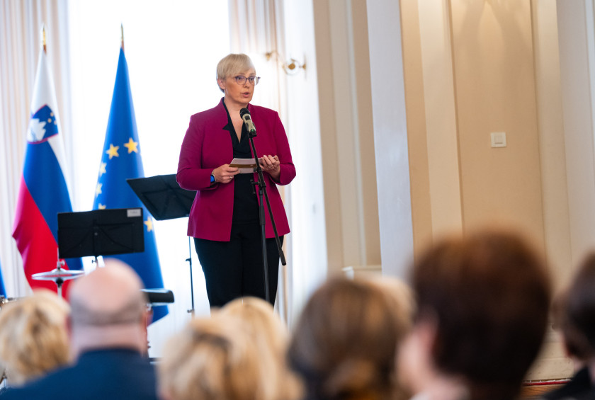 Predsednica za samostoječim mikrofonom nagovarja udeležence sprejema.