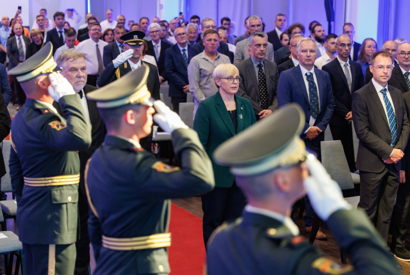 Predsednica in drugi udeleženci slovesnosti stojijo v dvorani in opazujejo pripadnike častne garde, ki imajo roke dvignjene k glavi.