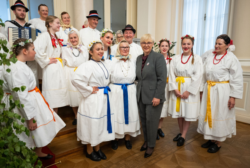 Predsednica stoji med folkloristi v belih narodnih nošah.