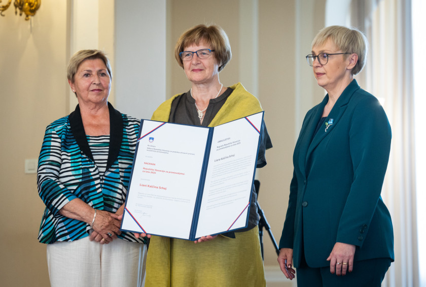 Nagrajenka v rokah drži veliko priznanje, na obeh straneh ima predstavnico podeljevalcev in predsednico.