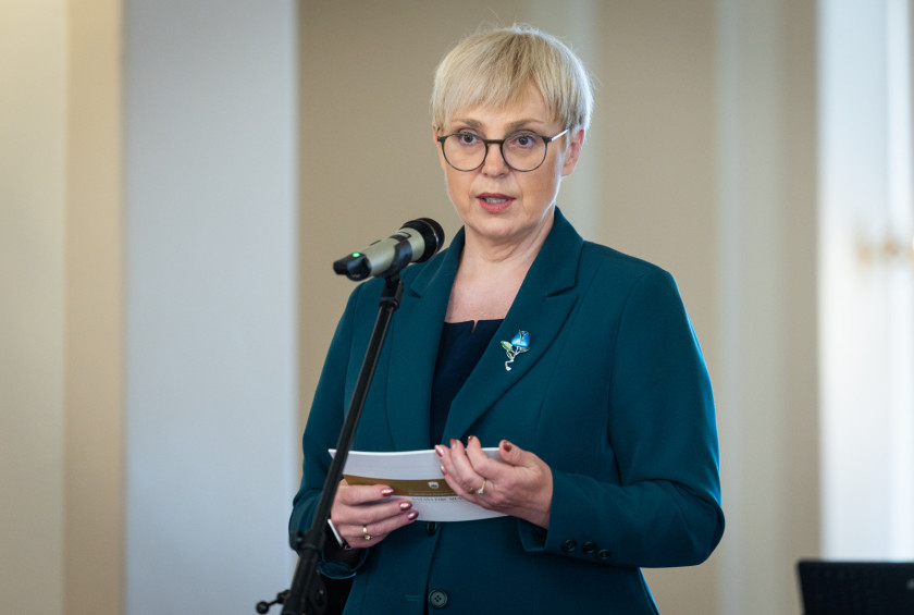 Predsednica v rokah drži govor in za mikrofonom nagovarja udeležence sprejema.