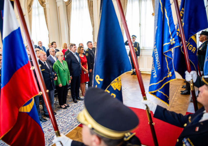 Nosilci praporjev stojijo pred udeleženci sprejema.