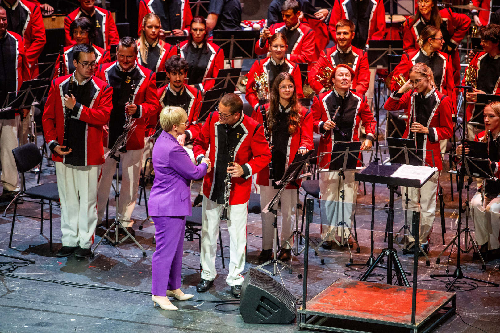 Predsednica se rokuje z glasbenikom Pihalnega orkestra Pošta Maribor na odru.