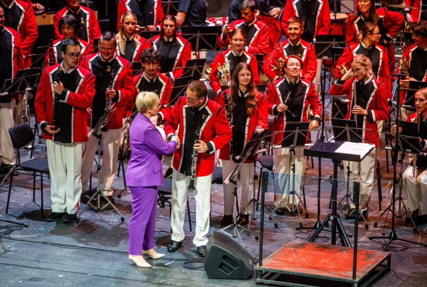 Predsednica se rokuje z glasbenikom Pihalnega orkestra Pošta Maribor na odru.