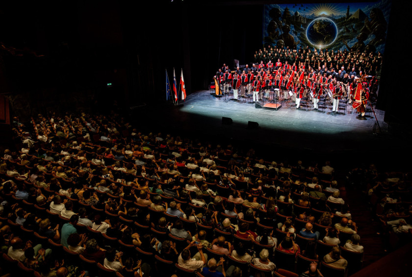 Koncert Pihalnega orkestra Pošta Maribor in občinstvo v dvorani.