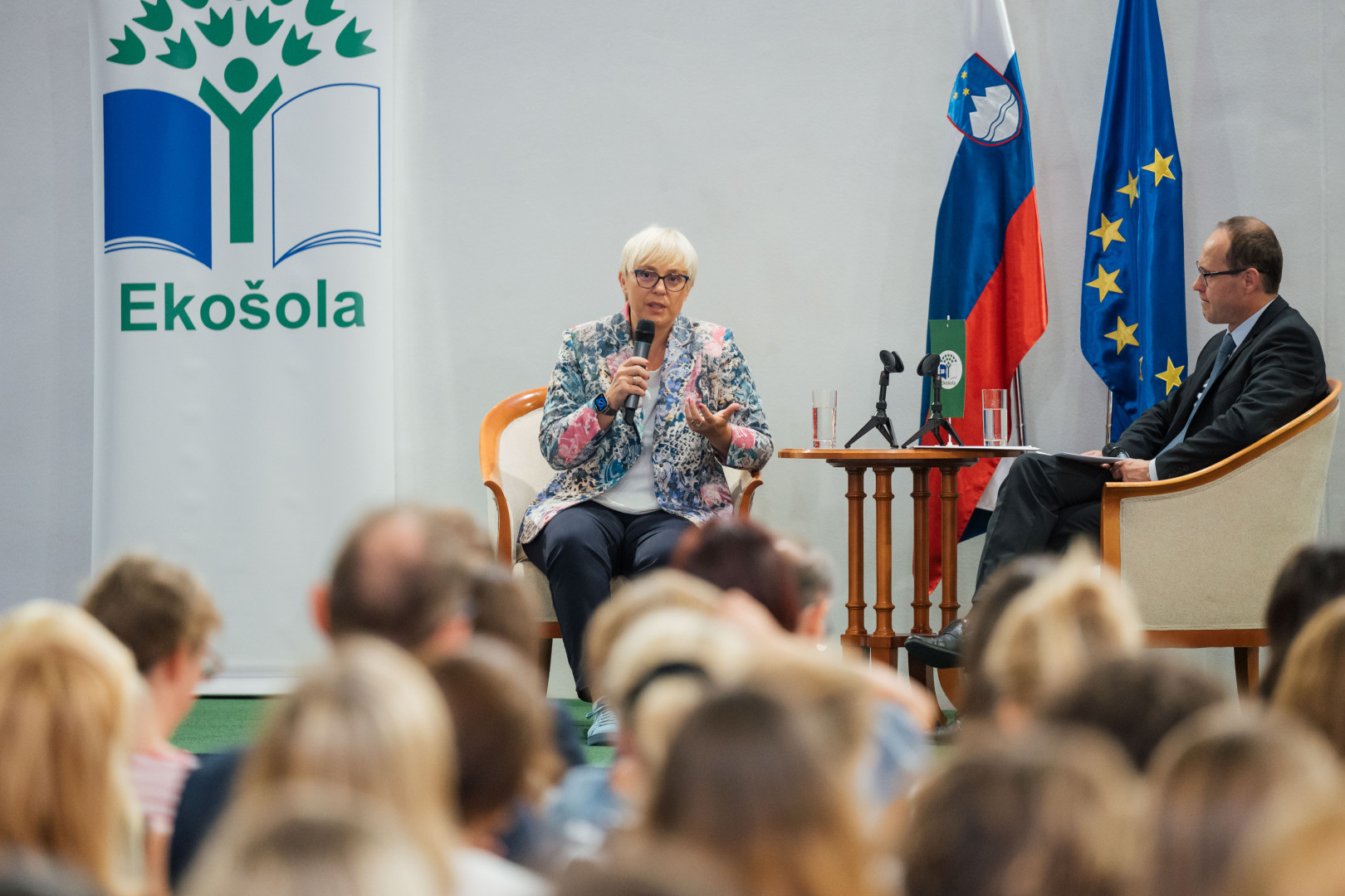 Predsednica sedi na odru in govori.
