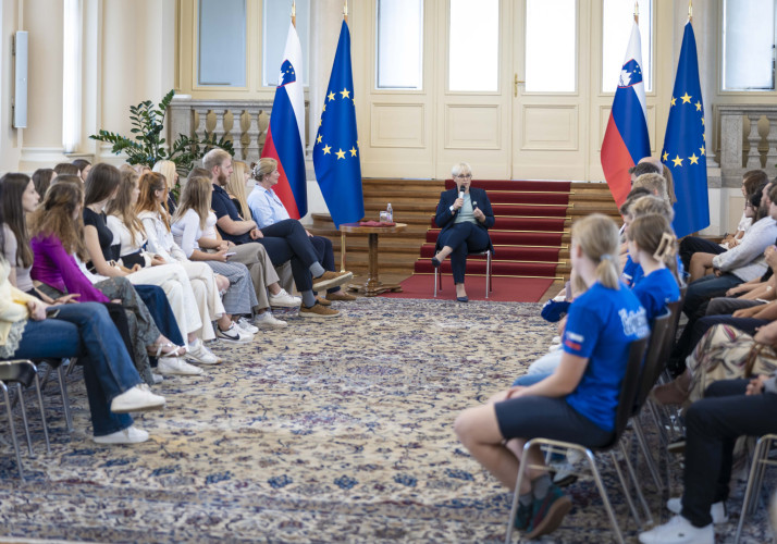Dijaki in učenci sedijo v polkrogu in spremljajo nagovor predsednice.