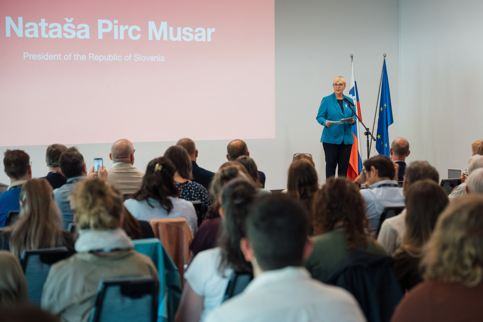 Predsednica stoji na odru in nagovarja zbrane na kongresu.