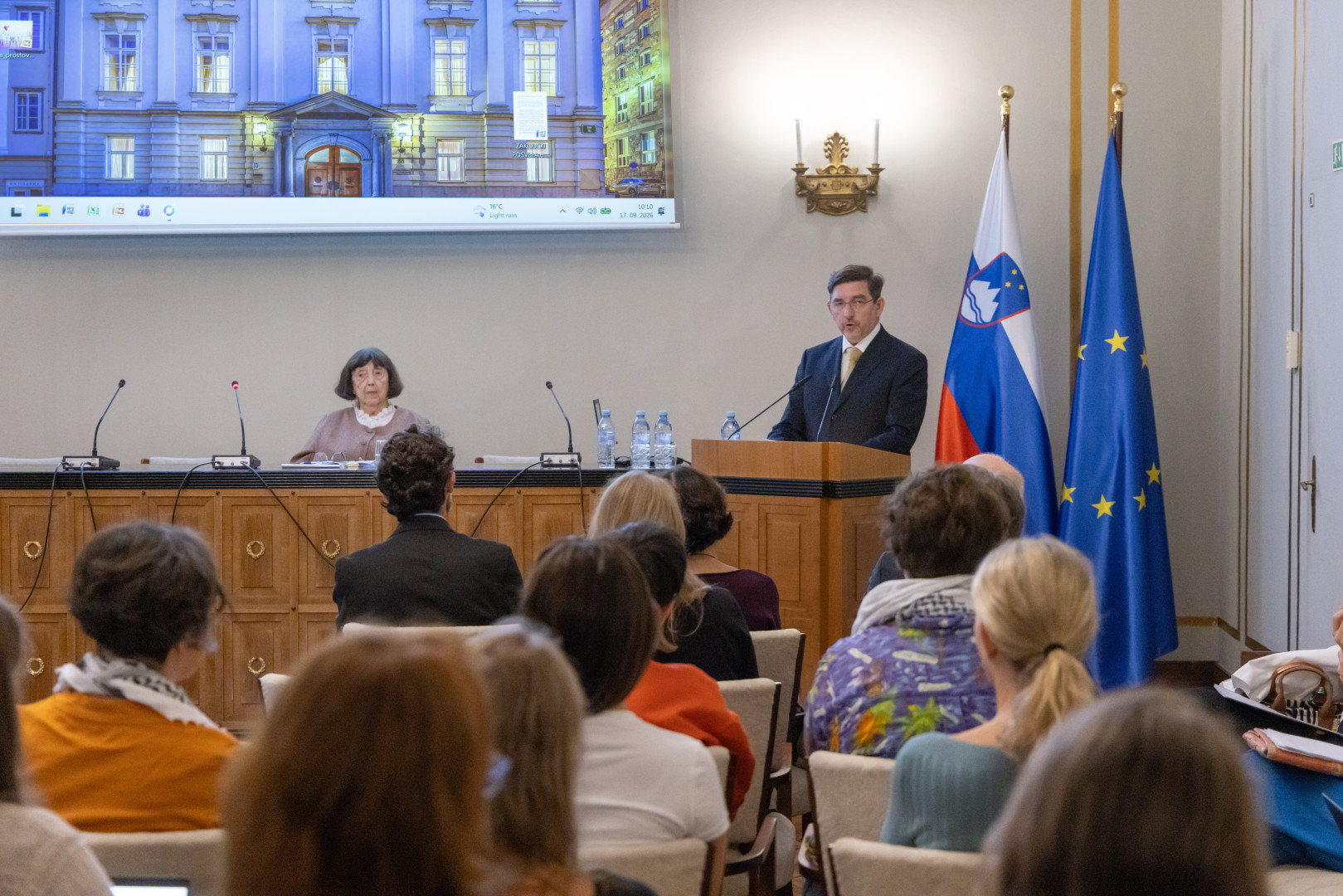 Dr. Aleš Musar govori za govorniškim pultom, v ozadju sta zastavi Slovenije in Evropske unije.
