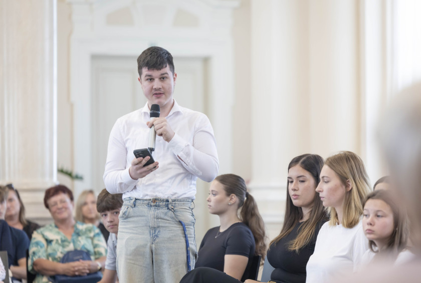 Učenec drži v roki mikrofon in zastavlja vprašanje predsednici.